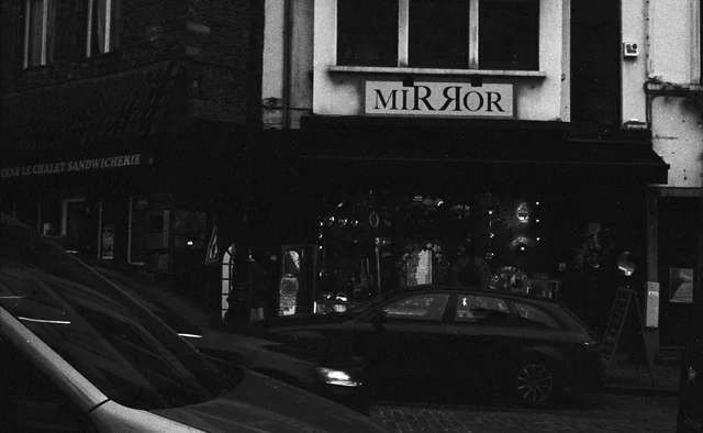 Parked cars outside a shadowed shopfront with a Mirror sign