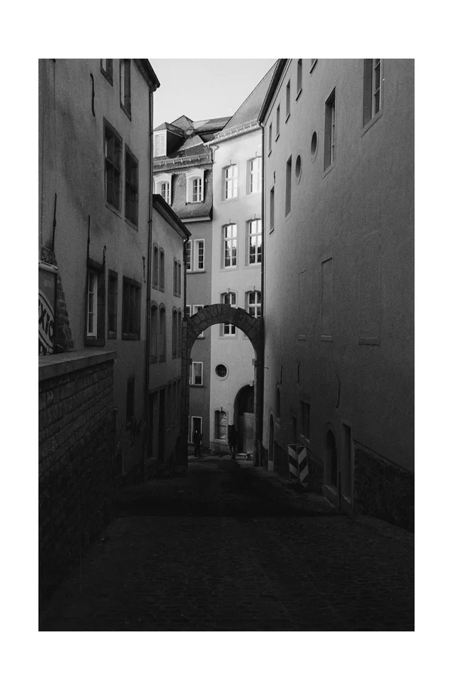 A narrow cobbled passage between tall buildings with an archway overhead