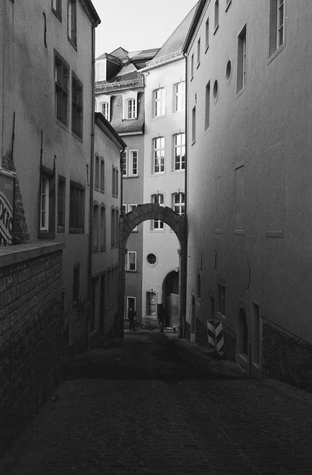 A narrow cobbled passage between tall buildings with an archway overhead