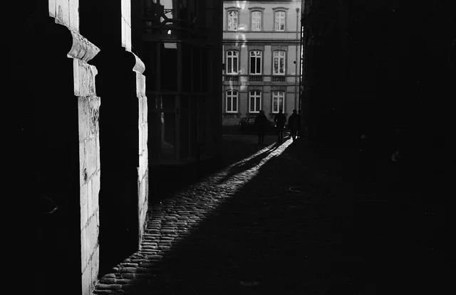 A shaft of sunlight crossing a dark cobbled passage lined with columns