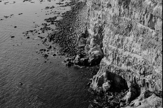 A steep rocky cliff meeting the sea along a narrow shoreline