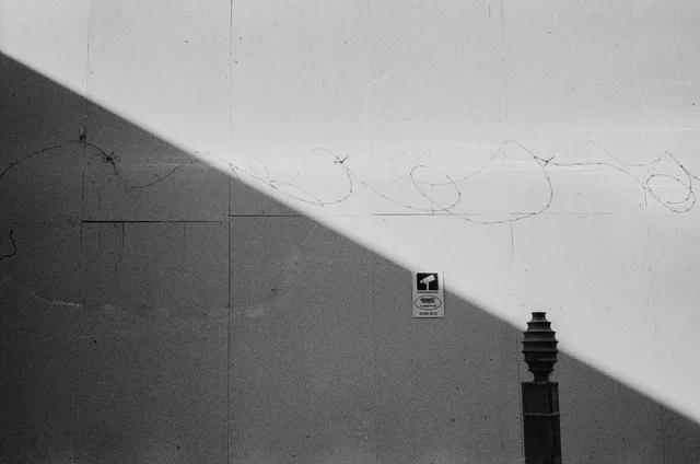 A diagonal shadow crossing a wall marked with faint graffiti beside a short bollard