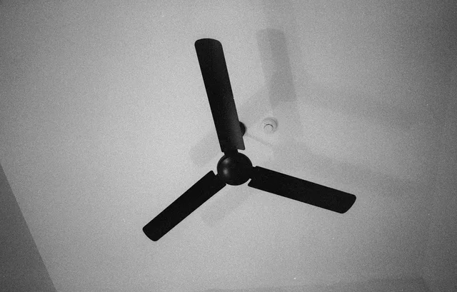 A three-bladed ceiling fan casting a faint shadow on a white ceiling