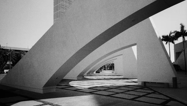 Repeating white arches above a tiled walkway striped with sunlight and shadow