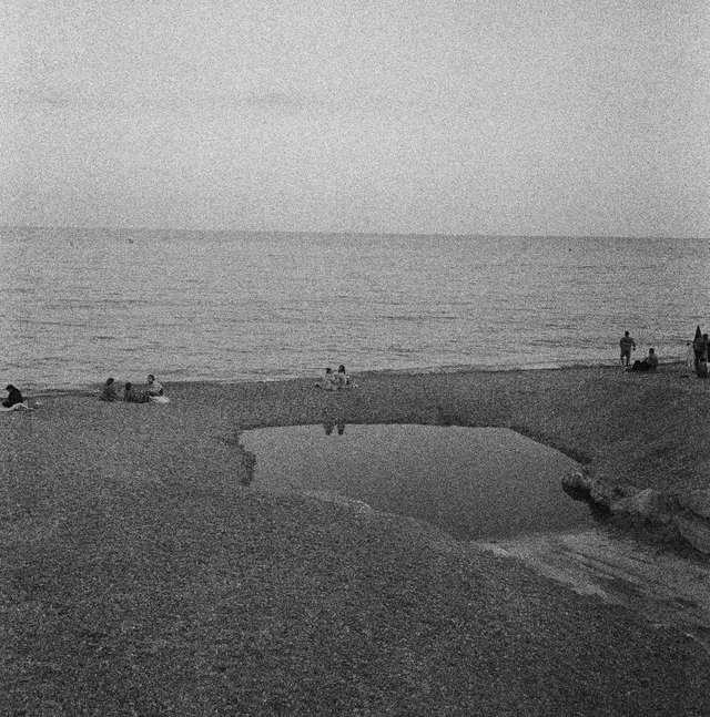 People scattered along a rocky seafront around a shallow pool