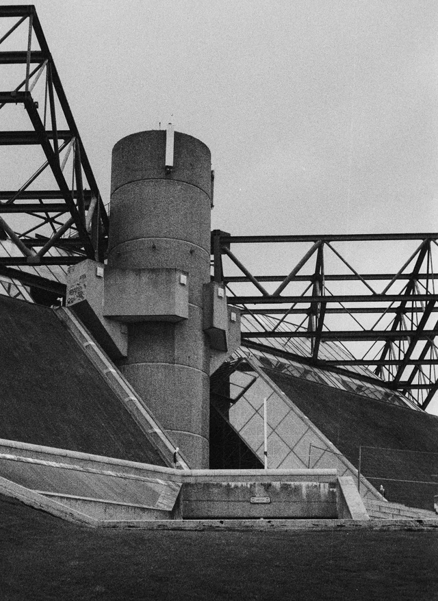 A cylindrical concrete tower surrounded by angular walls and exposed steel trusses