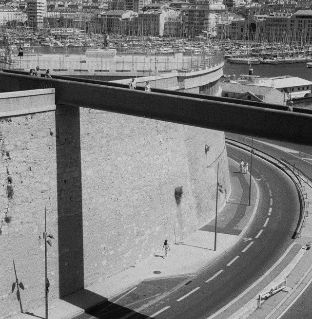 An elevated view of a curving road beneath a high stone wall