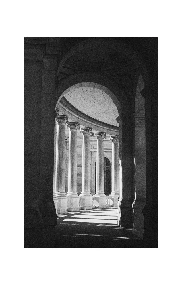 Sunlight entering a curved stone colonnade through tall arches