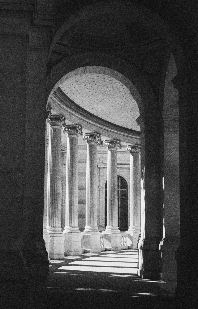 Sunlight entering a curved stone colonnade through tall arches