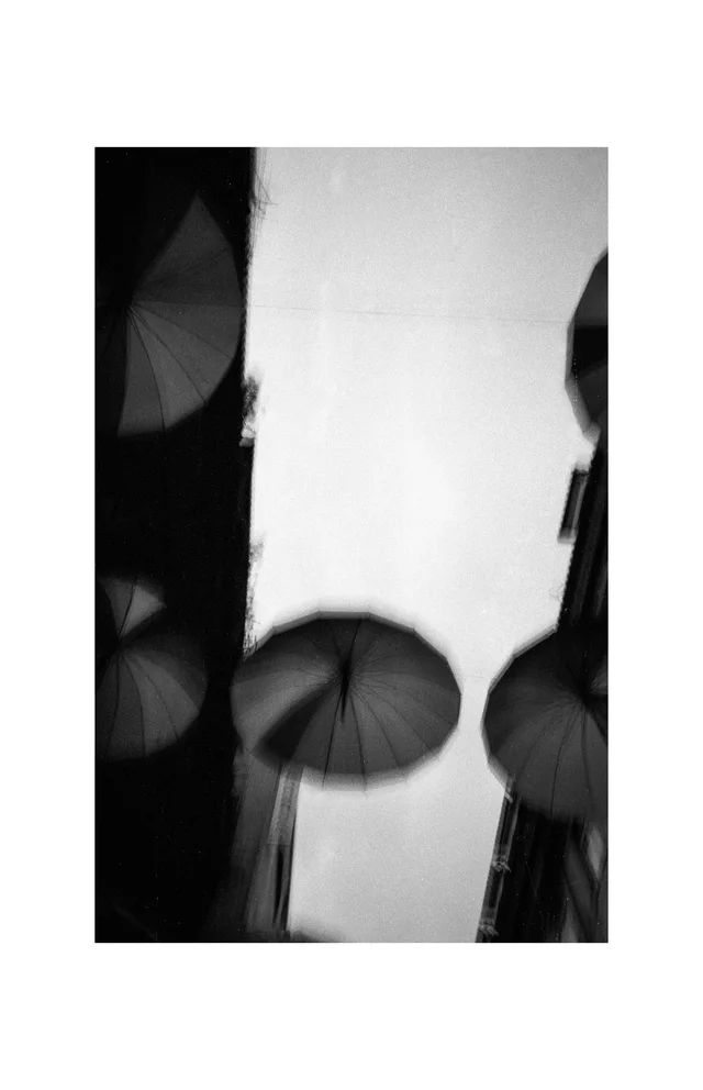 Umbrellas suspended above a narrow passage between dark buildings