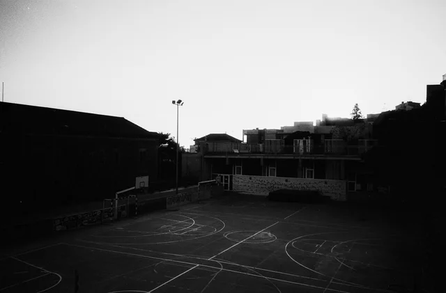 An empty outdoor sports court in deep shadow below surrounding buildings