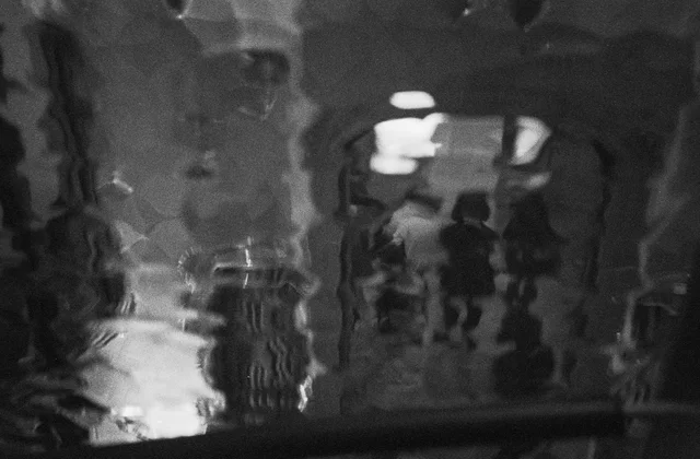 Distorted reflections of figures and lights across a rippling surface