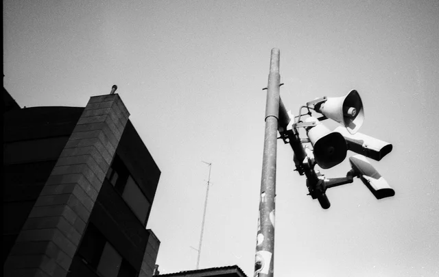 A cluster of traffic signals on a pole beside an angular building