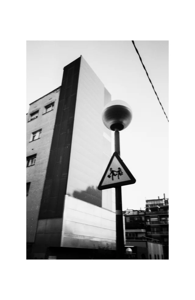 A rounded streetlamp and triangular crossing sign beside a sharply angled building