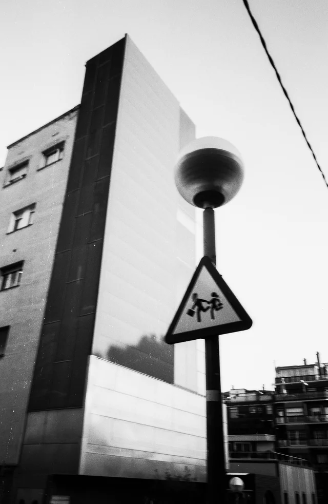 A rounded streetlamp and triangular crossing sign beside a sharply angled building
