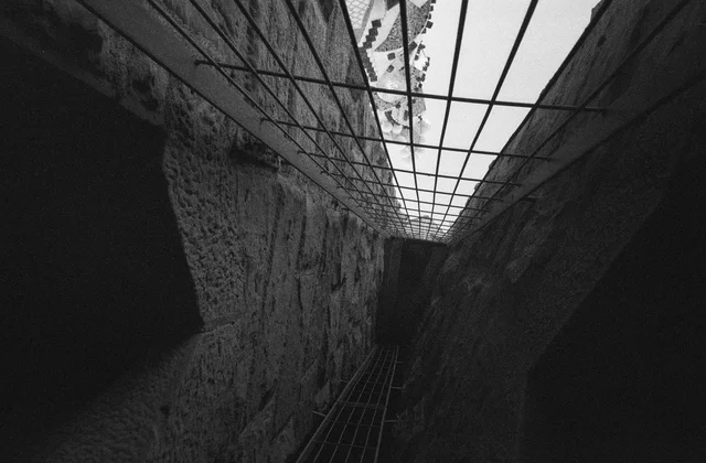 Looking upward through a narrow rough-walled shaft beneath a metal grid
