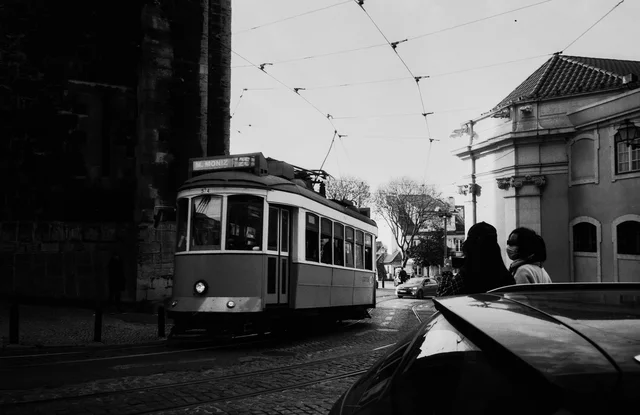 A tram on cobbled tracks beneath overhead wires, with pedestrians nearby