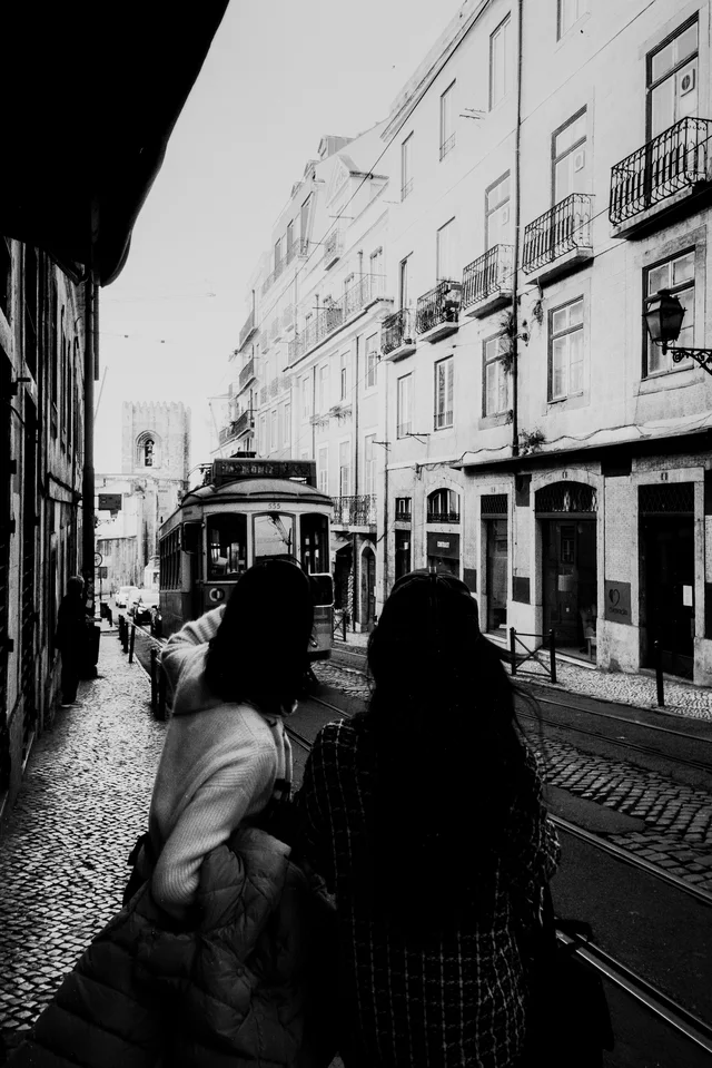 Two people walking along a narrow street toward an approaching tram