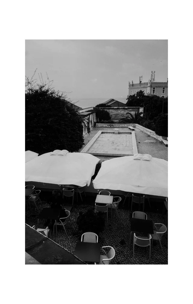 Cafe tables beneath pale umbrellas overlooking a long stone basin and a classical pavilion