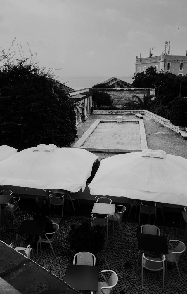 Cafe tables beneath pale umbrellas overlooking a long stone basin and a classical pavilion