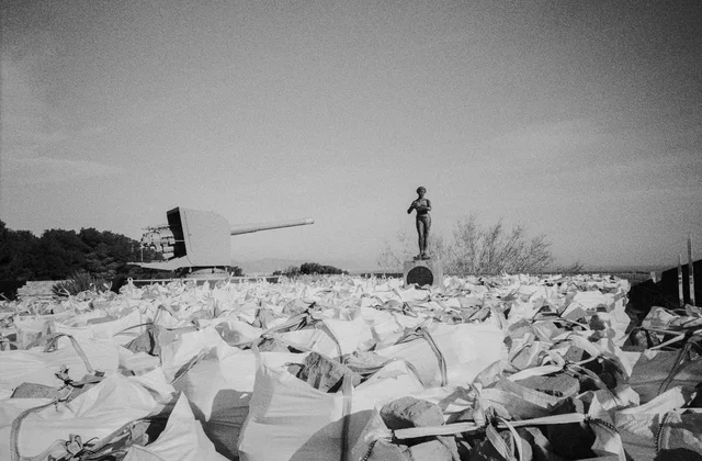 White sacks of stone beneath a cannon and a standing statue