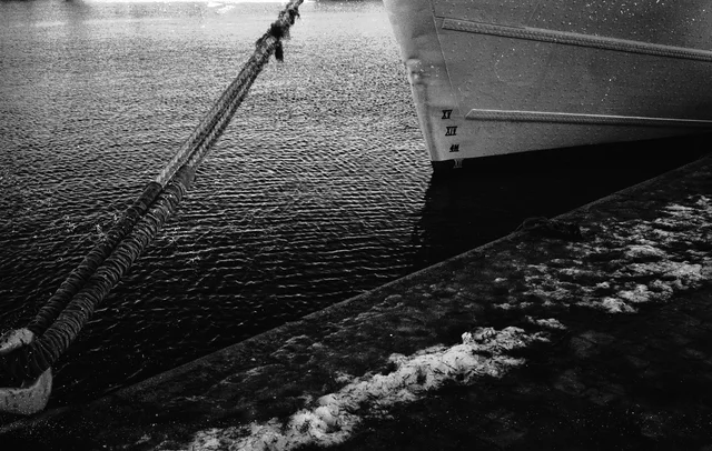 A thick mooring rope beside a boat and a snow-dusted quay