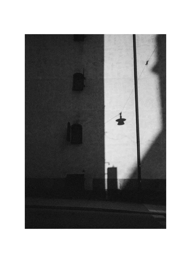 A hanging streetlamp silhouetted against a sunlit strip of a tall wall