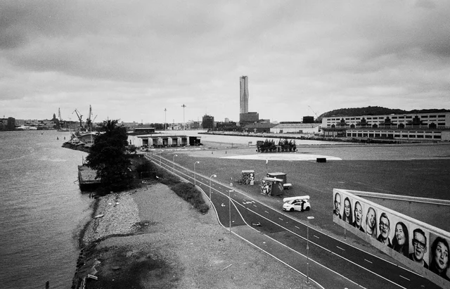 A waterfront cycle path beside an open paved area and a long mural of faces