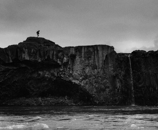 A lone figure atop layered cliffs above a river