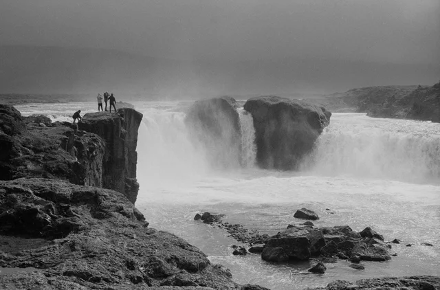 People standing on a rocky ledge beside a broad waterfall