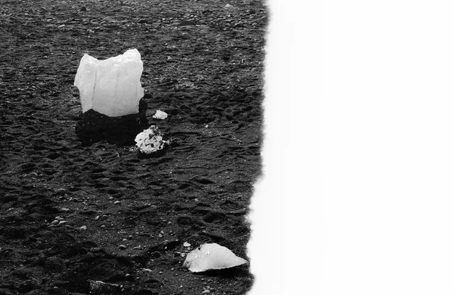 A large piece of ice and smaller fragments resting on dark sand