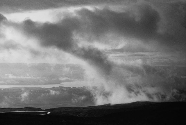 A pale plume rising from dark open ground beneath heavy clouds
