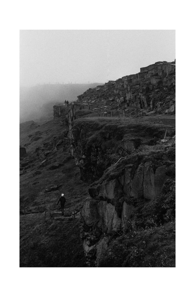 A lone walker on a narrow path beneath mist-covered rocky cliffs
