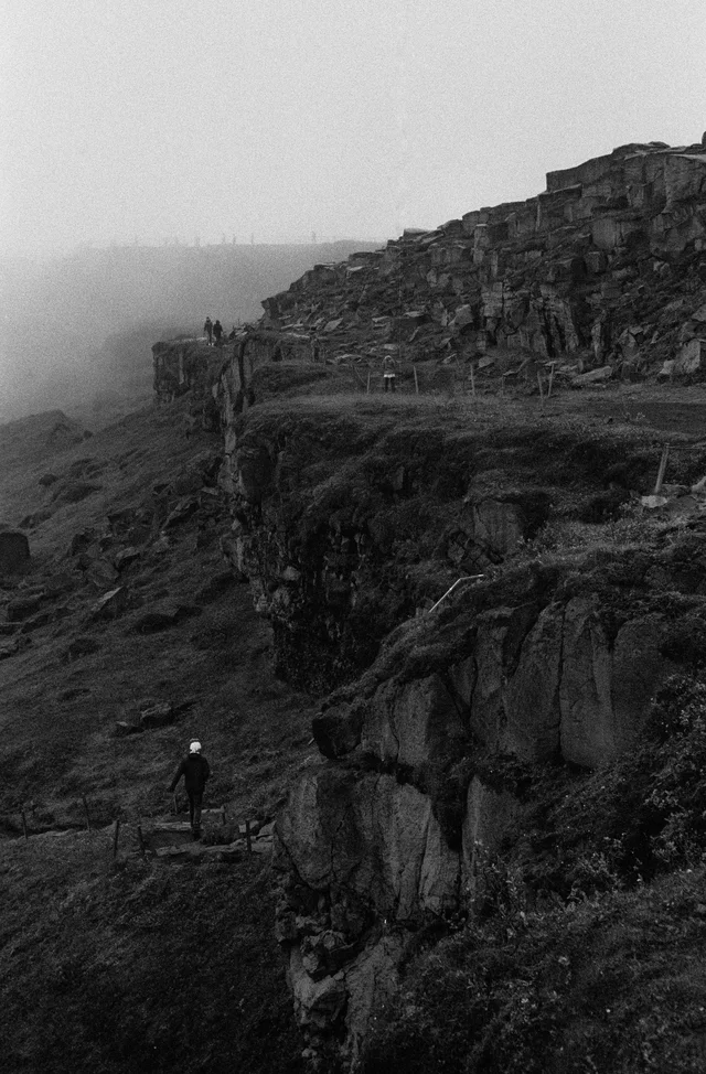A lone walker on a narrow path beneath mist-covered rocky cliffs