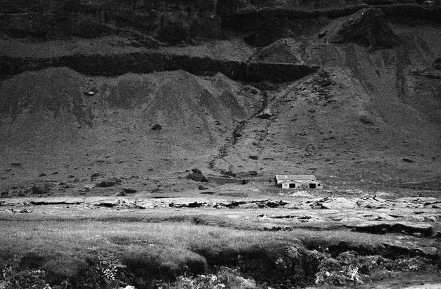 A small camper van on an open plain beneath a steep mountain slope