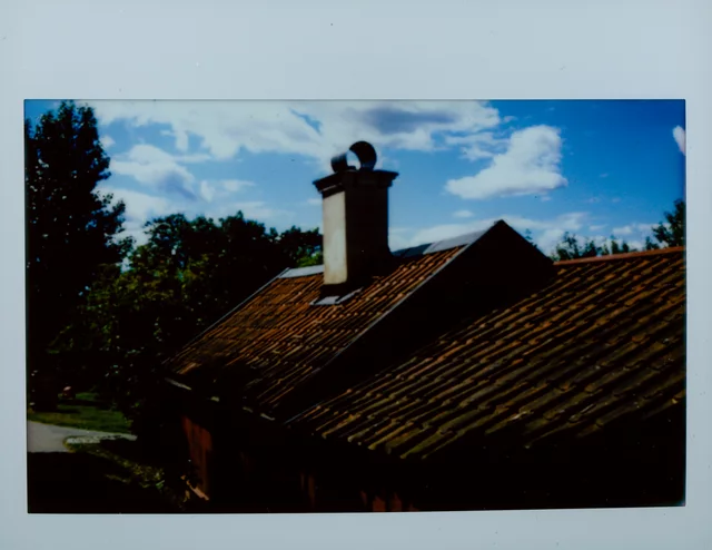 A chimney rising from a tiled roof against a blue sky and white clouds