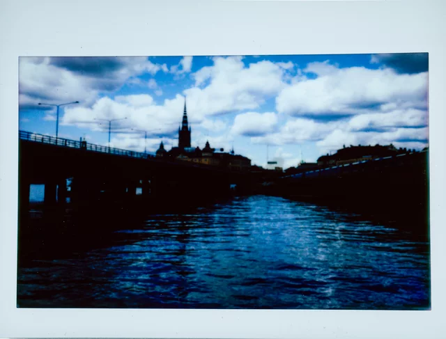 Blue water below a dark waterfront skyline and a church spire beneath scattered clouds