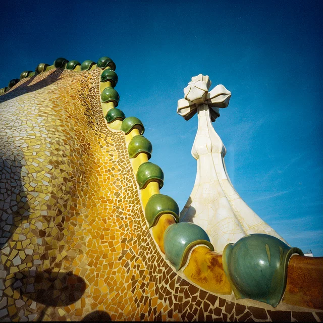 A yellow mosaic wall edged with green ceramic spheres beside a sculpted cross