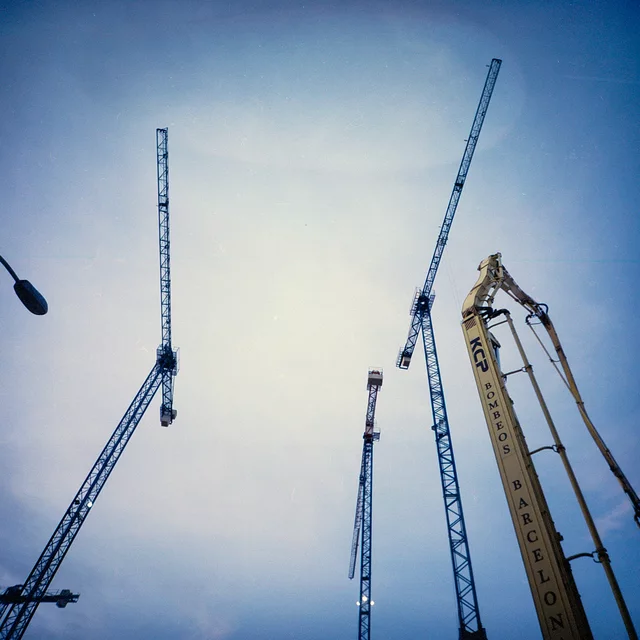 Tall construction cranes reaching into a pale blue sky