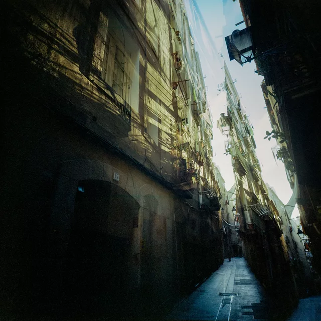 A narrow alley with shadowed doorways and sunlit upper walls