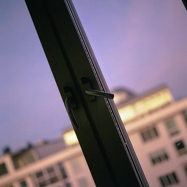 An open window and handle framing a building beneath a purple sky