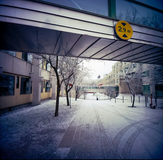 A covered passage opening onto a snowy courtyard beneath a yellow clearance sign