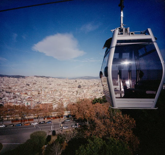 A cable car suspended above a sprawling city beneath a blue sky