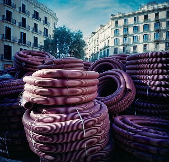 Coils of pink corrugated tubing stacked along a city street