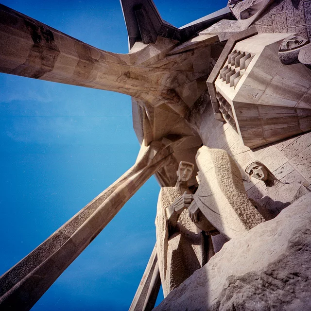 Carved stone figures and angular supports viewed from below against a blue sky