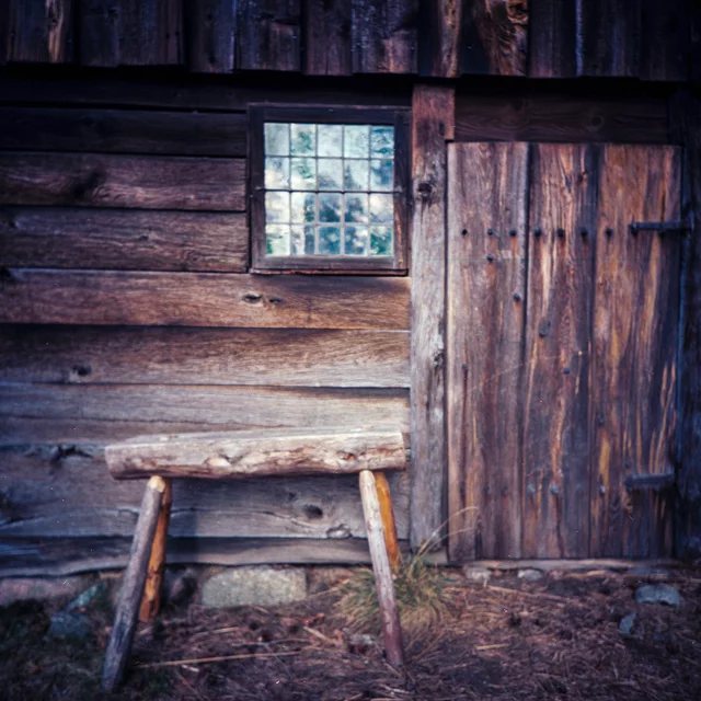 A small wooden stool beneath a window in a weathered timber wall