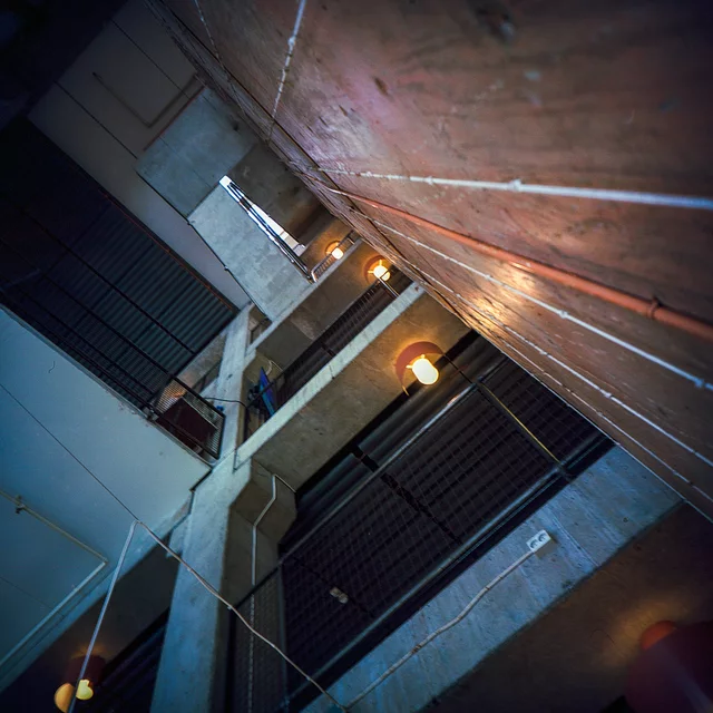An angular concrete stairwell viewed from below, with warm ceiling lights