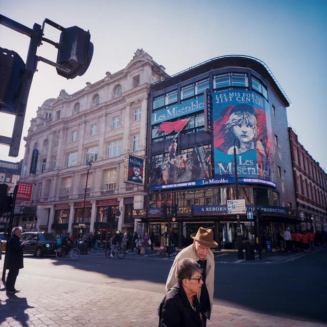 Pedestrians in front of a theatre with a large Les Misérables poster