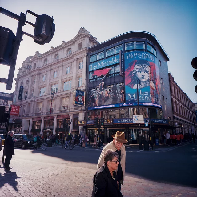 Pedestrians in front of a theatre with a large Les Misérables poster
