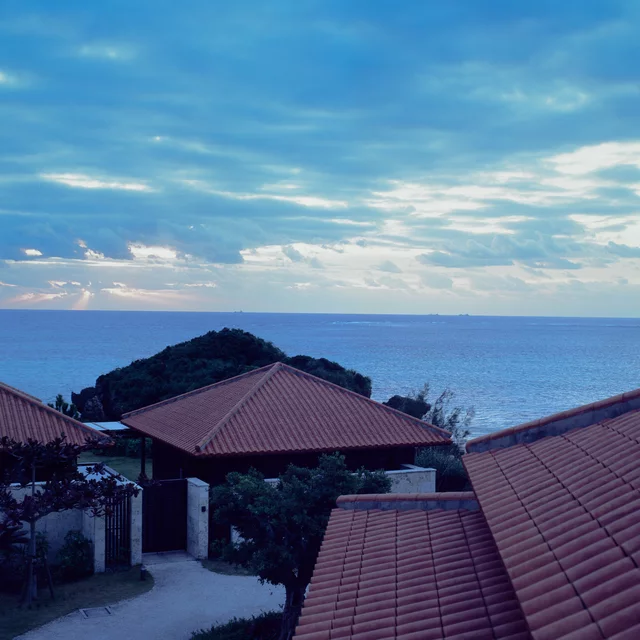 Red-tiled roofs overlooking blue sea beneath a cloud-filled sky